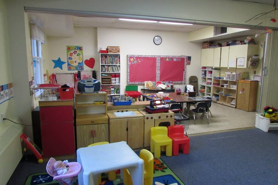 Classroom with small tables and chairs, bookshelves, and red bulletin boards
