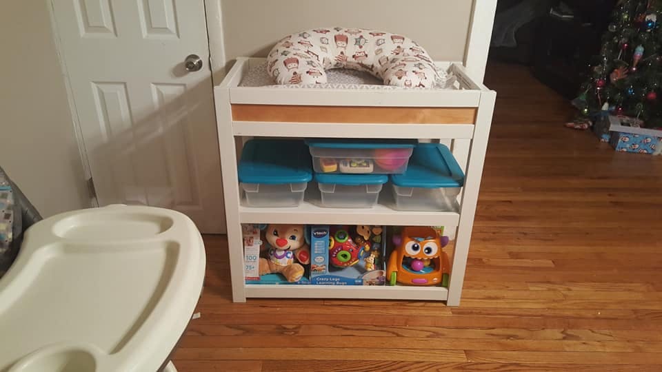 Changing table with a pillow, storage bins, and toys