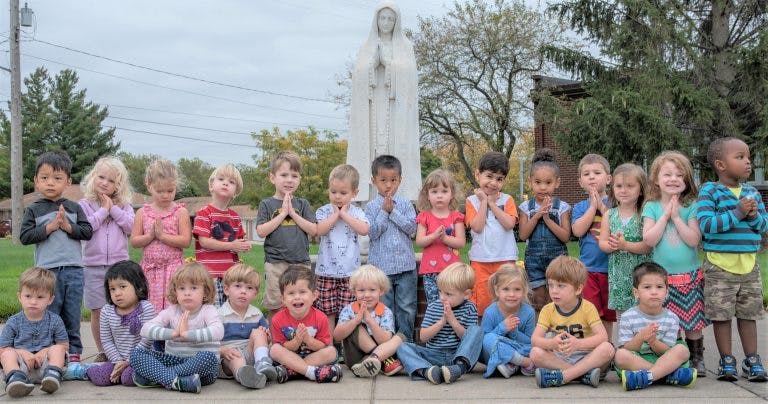 Group of children standing and sitting with hands together in prayer position