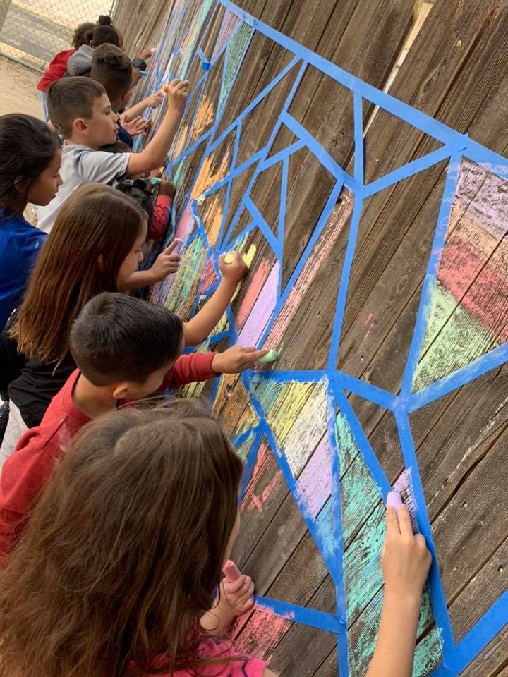 Children coloring on a wooden wall with chalk and blue tape