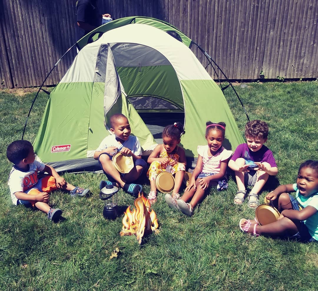 Children sitting in front of a tent with a pretend campfire