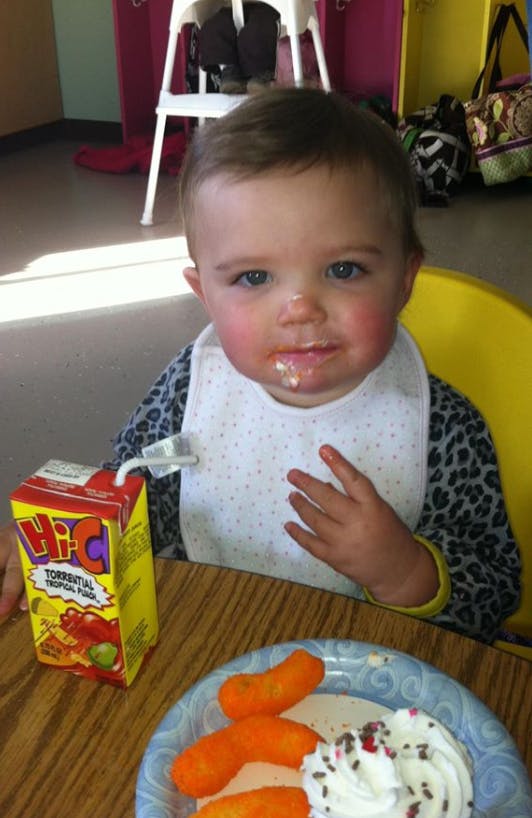 Child in a high chair with a bib, juice box, and food on a plate