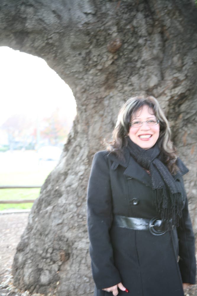 Person in a black coat and scarf standing in front of a large tree trunk