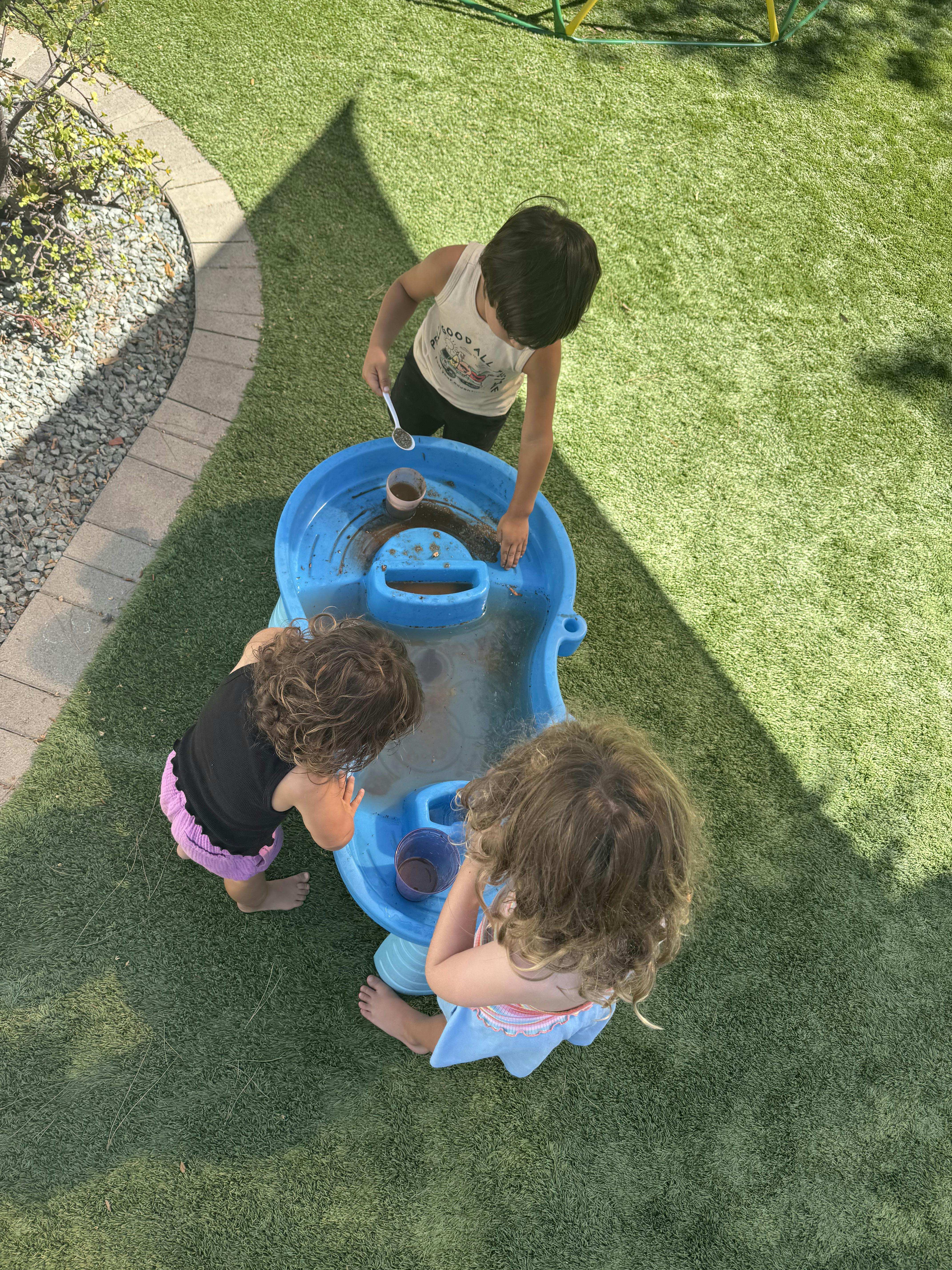 Three children playing with a blue water table on grass