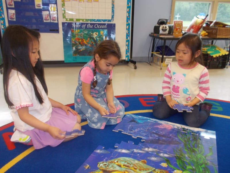 Three children kneeling on a rug, assembling a large floor puzzle