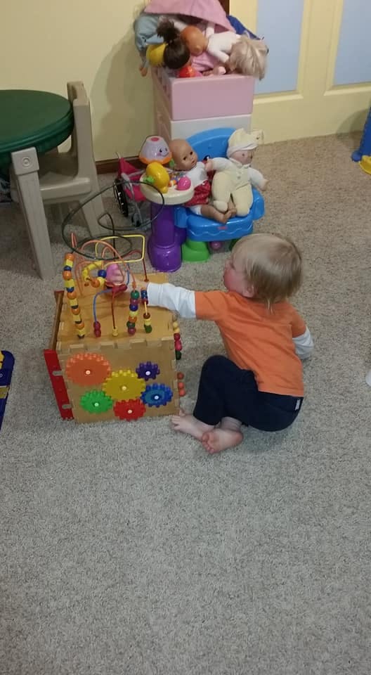 Child playing with a wooden activity cube on a carpeted floor