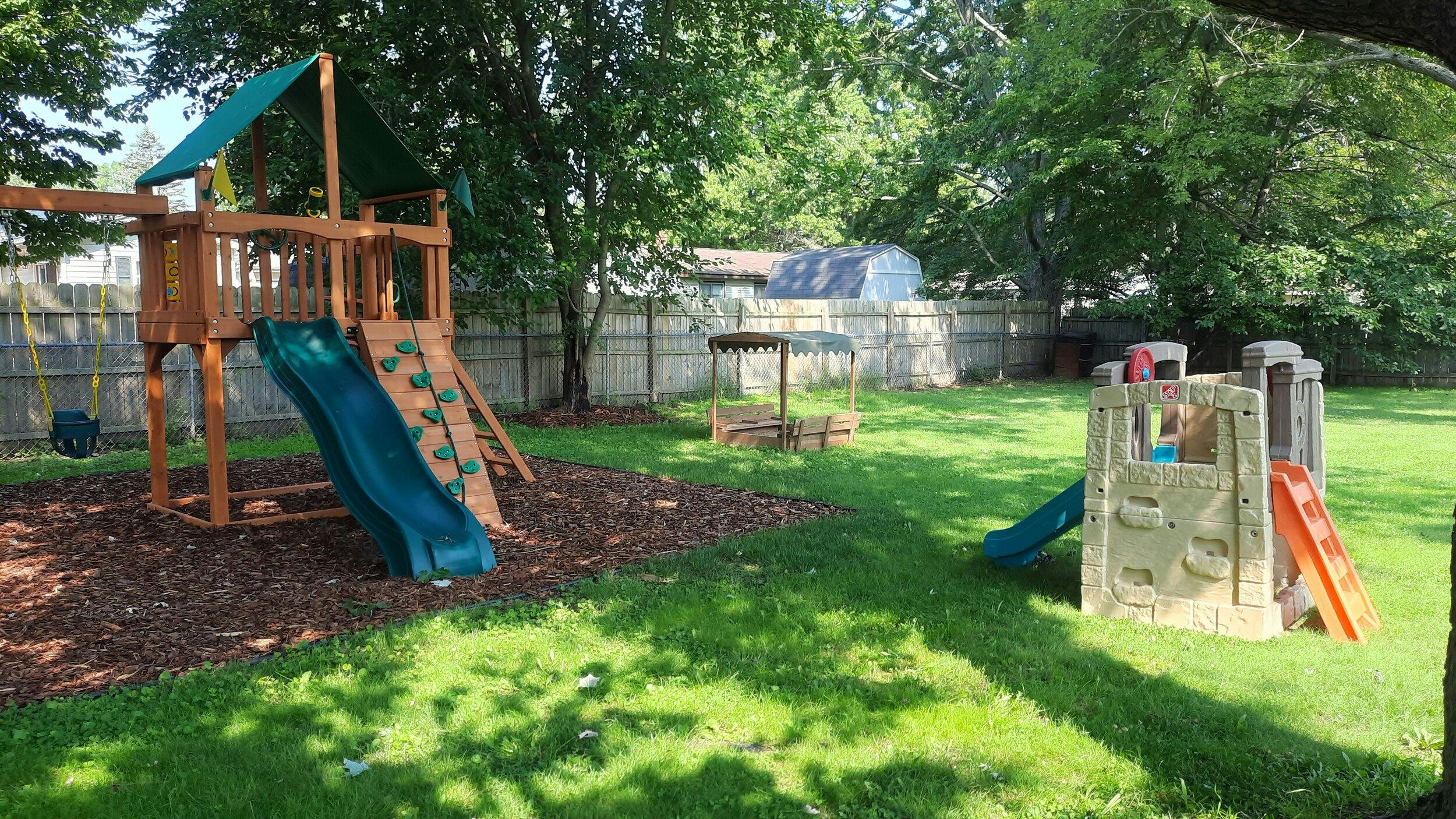 Backyard playground with wooden playset and plastic playhouse