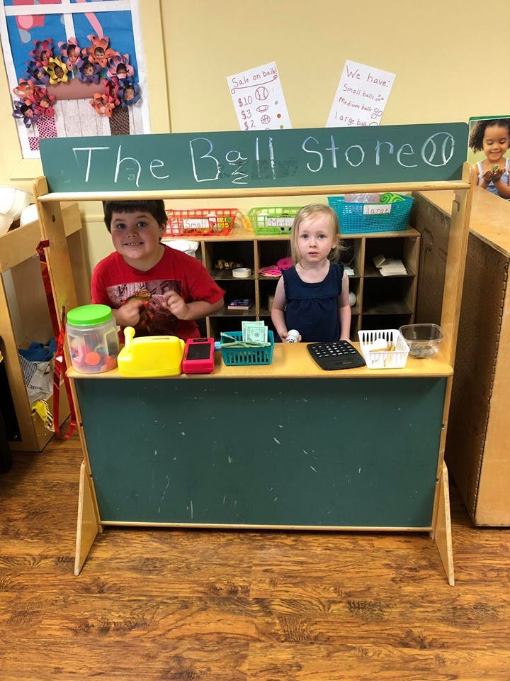 Two children playing in a pretend store with a sign that reads "The Ball Store"