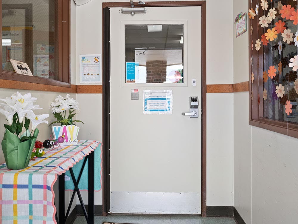 A beige door with a window and digital lock, next to a table with flowers