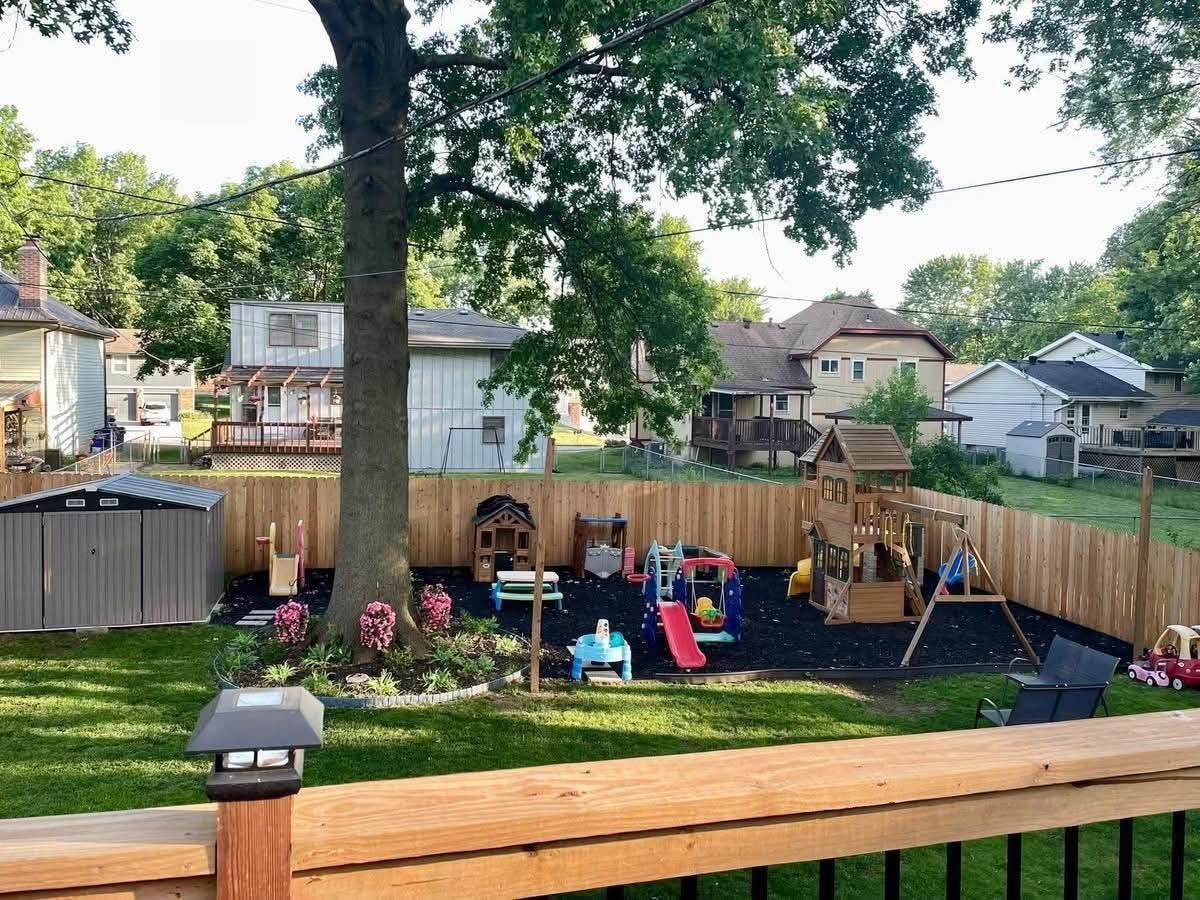 backyard with a wooden privacy fence, a large tree, and a children's play area