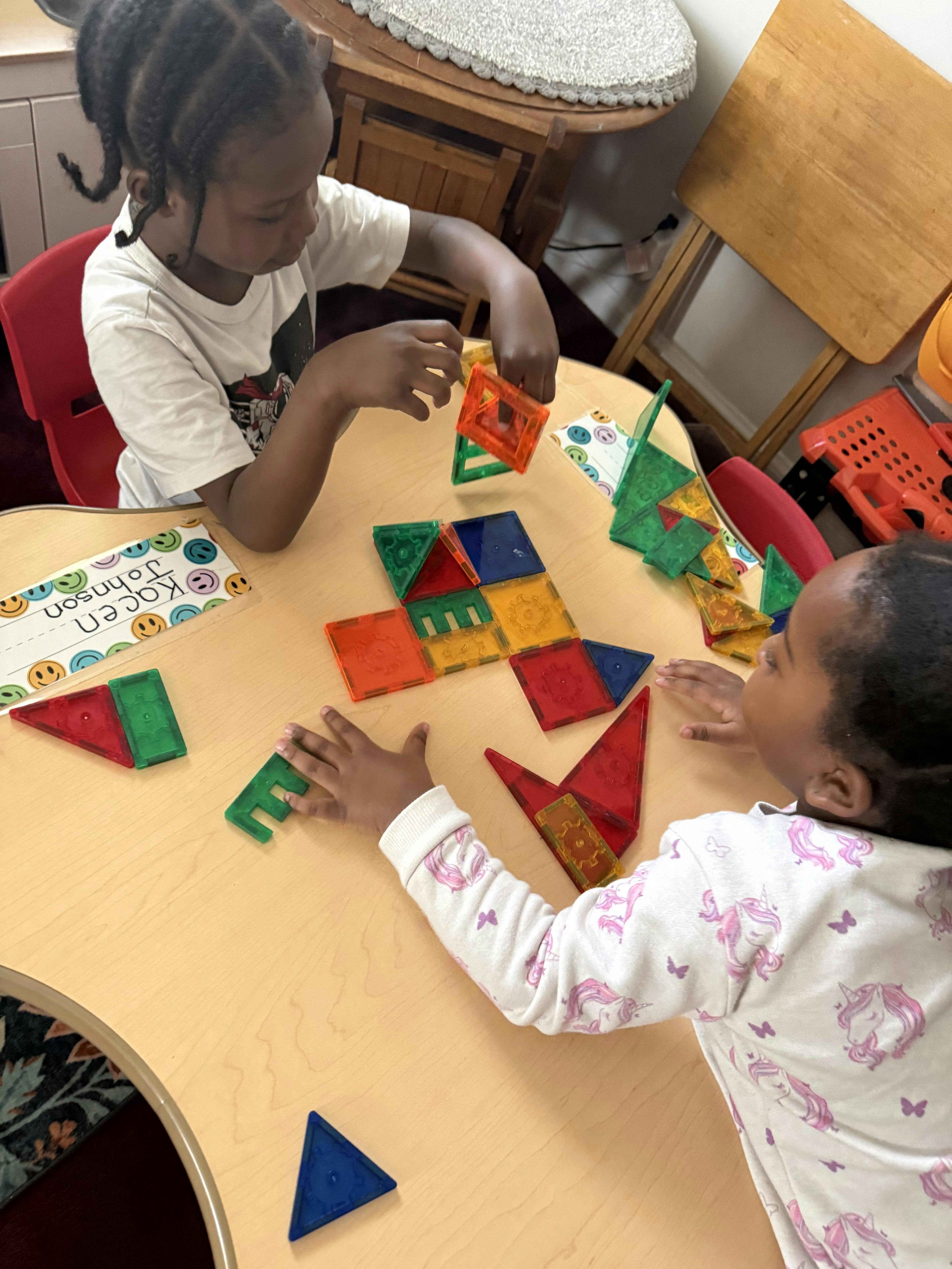 Two children playing with colorful magnetic blocks at a table