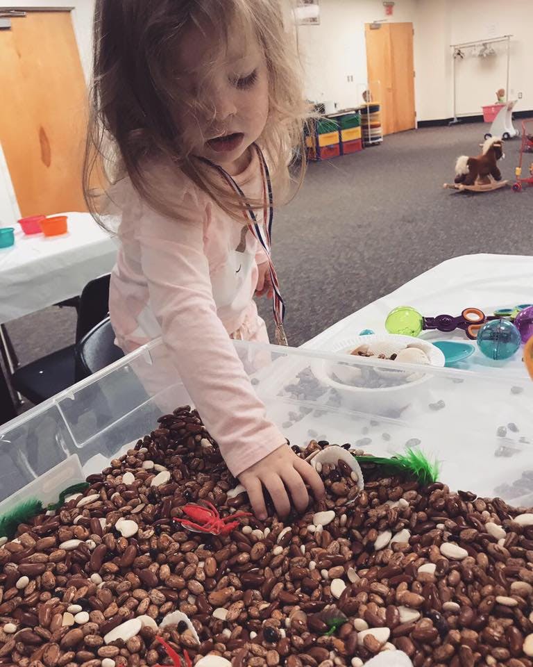 Child playing with beans and small toys in a sensory bin