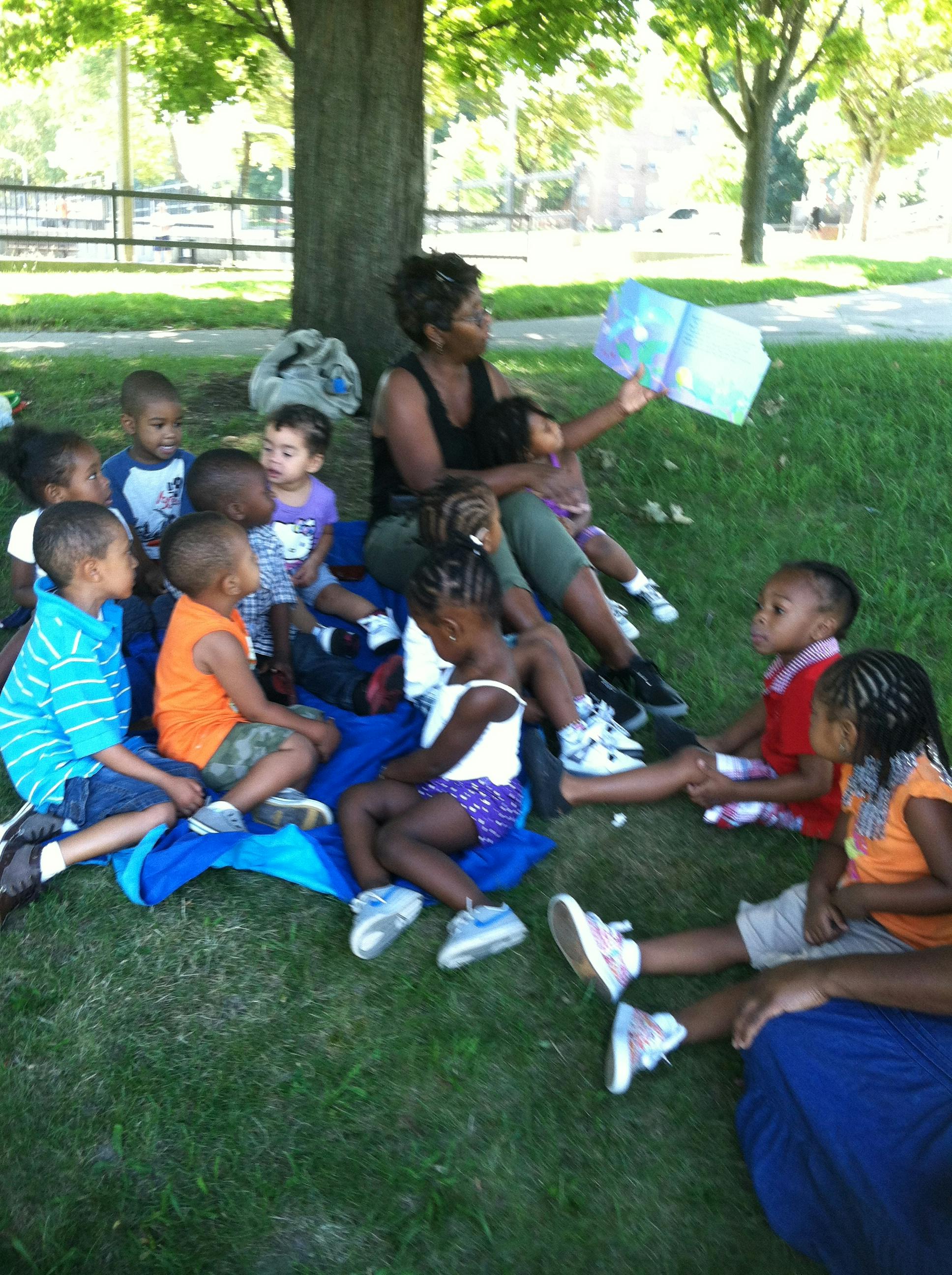 Adult person reading a book to a group of children outdoors