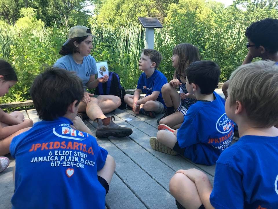 Person showing a card to a group of children sitting in a circle outdoors