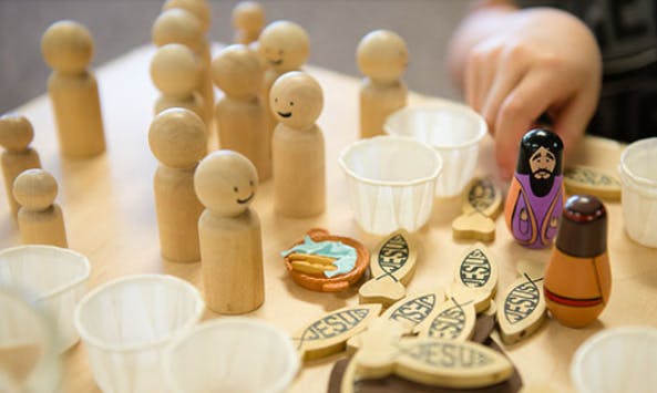 Child's hand reaching for wooden peg dolls and religious-themed items