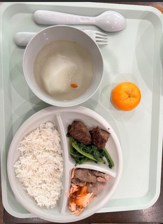 A divided plate with rice, beef, greens, and salmon, with a bowl of soup and an orange
