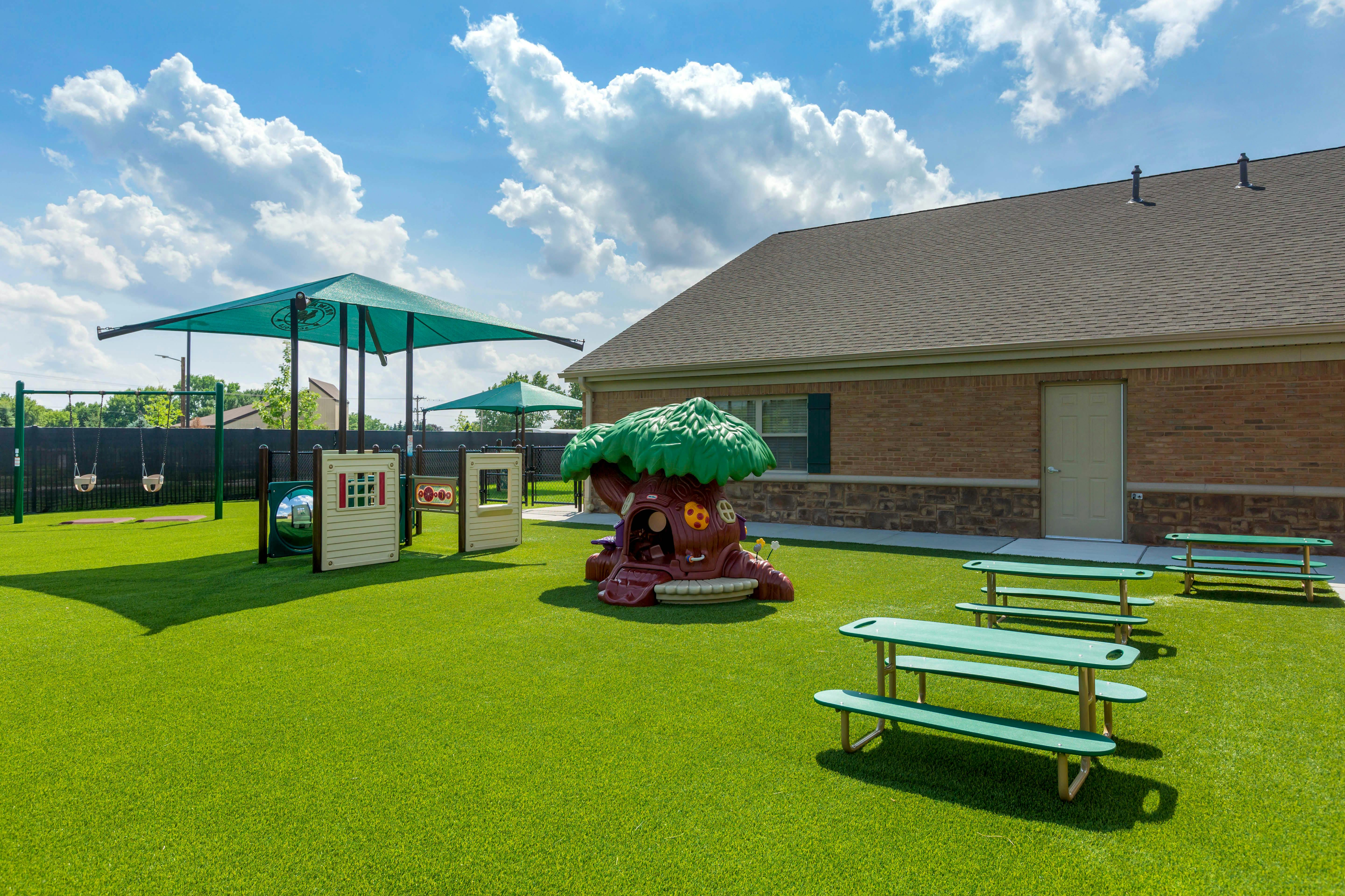 Outdoor playground area with swings, play structures, and green picnic tables
