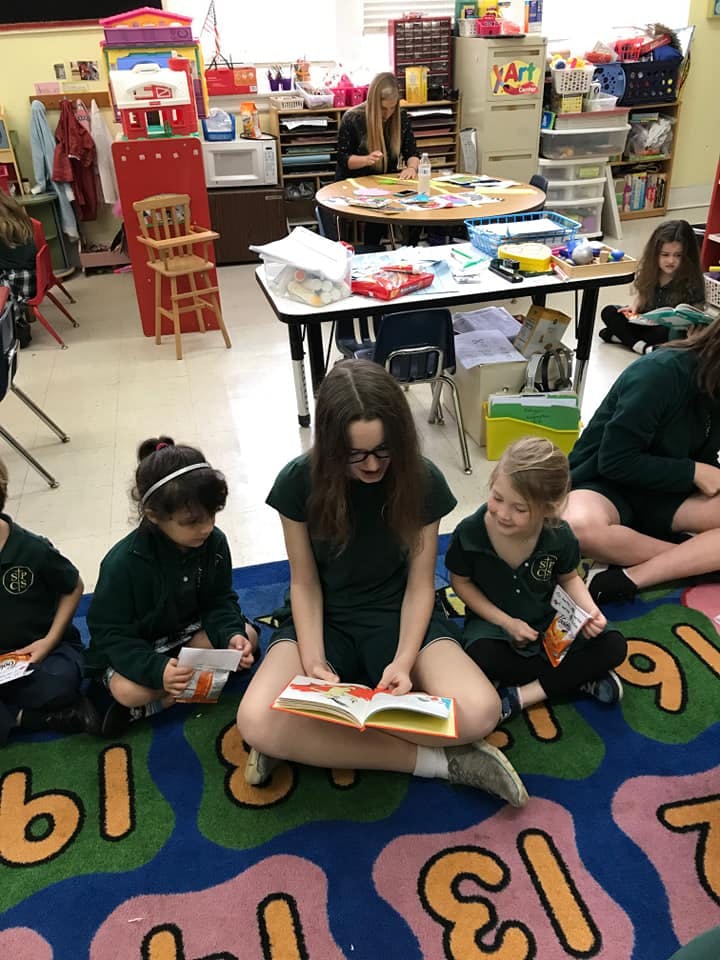 People and children sitting on a rug reading books in a classroom