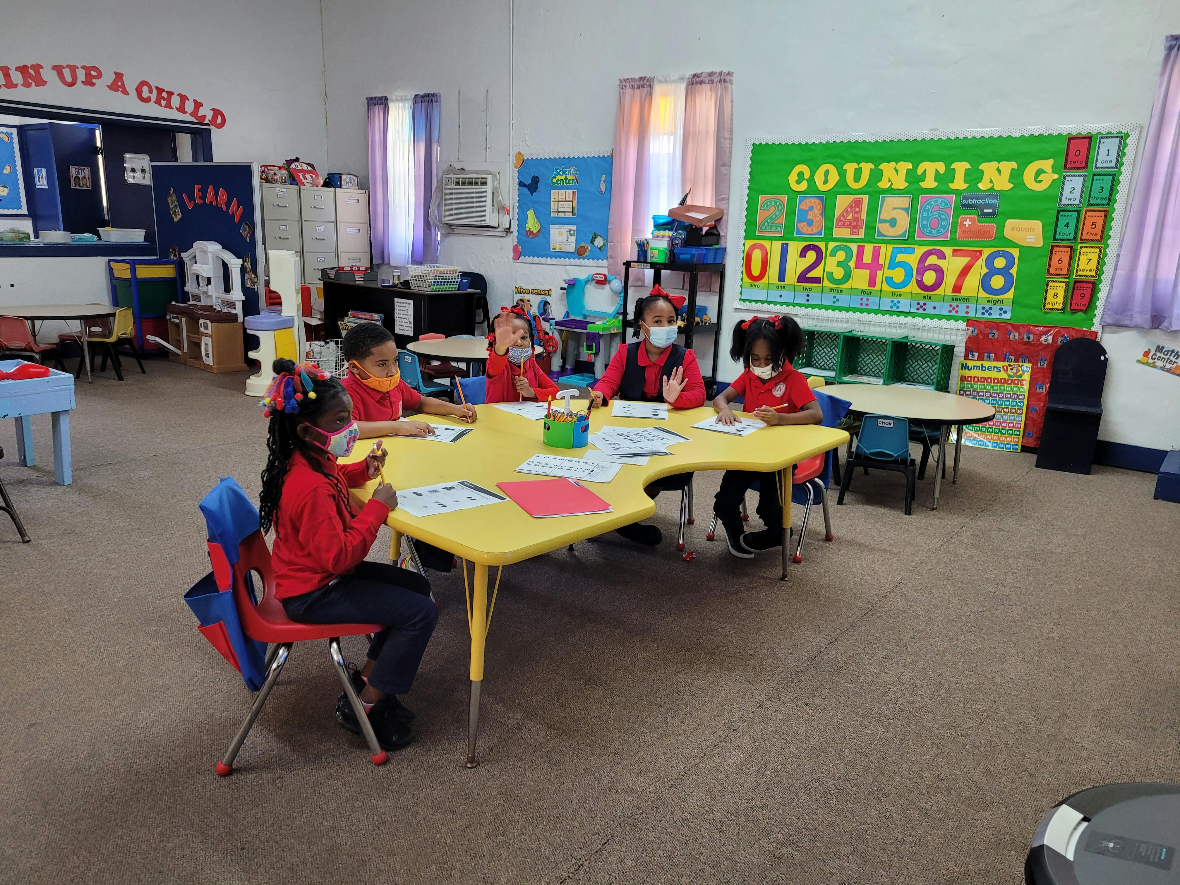 Children sitting at a yellow table in a classroom