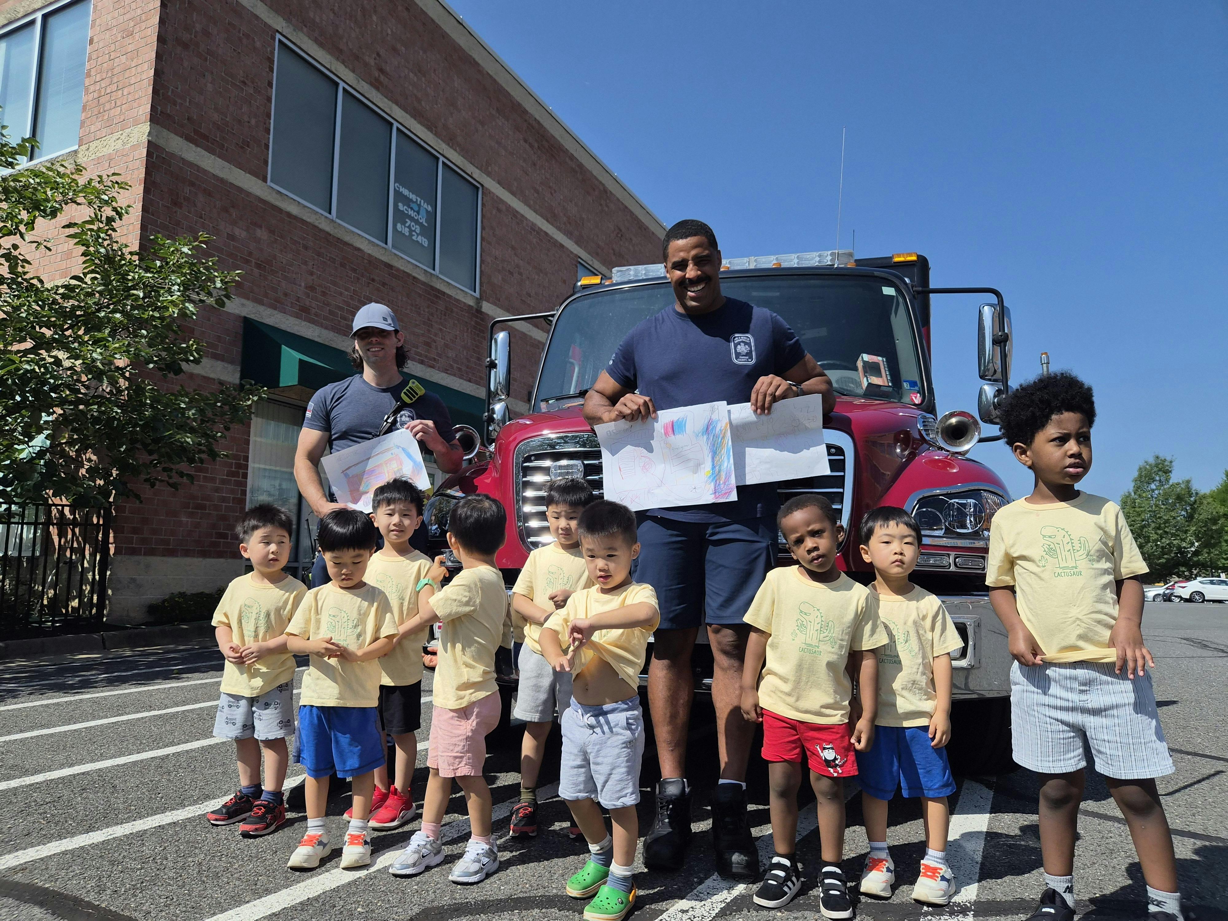 Group of children and adults standing in front of a fire truck holding drawings
