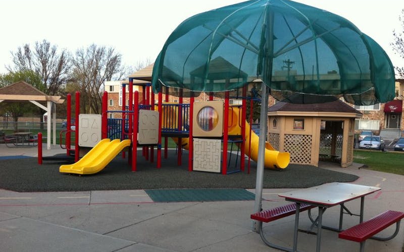 A playground with yellow slides, red posts, and a nearby picnic table with an umbrella