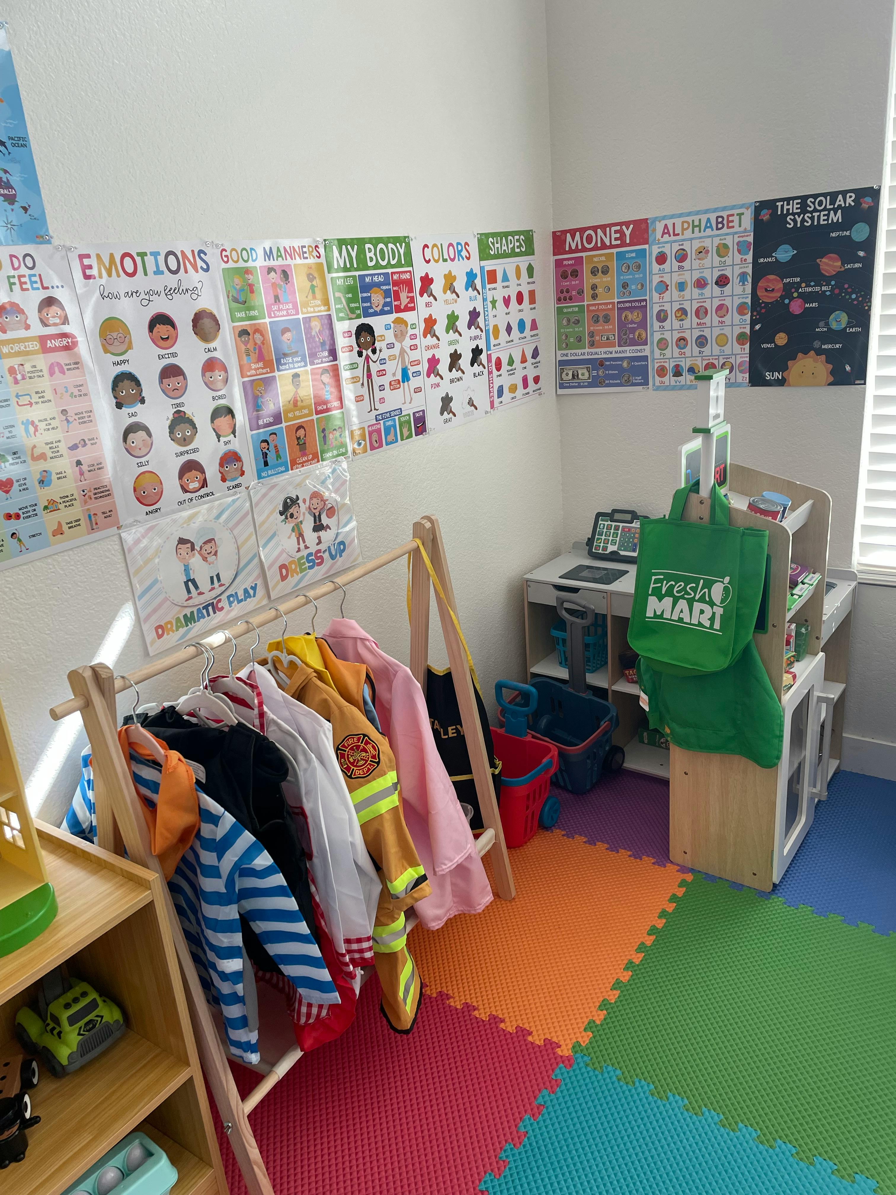 Classroom with educational posters, dress-up clothes, and play kitchen