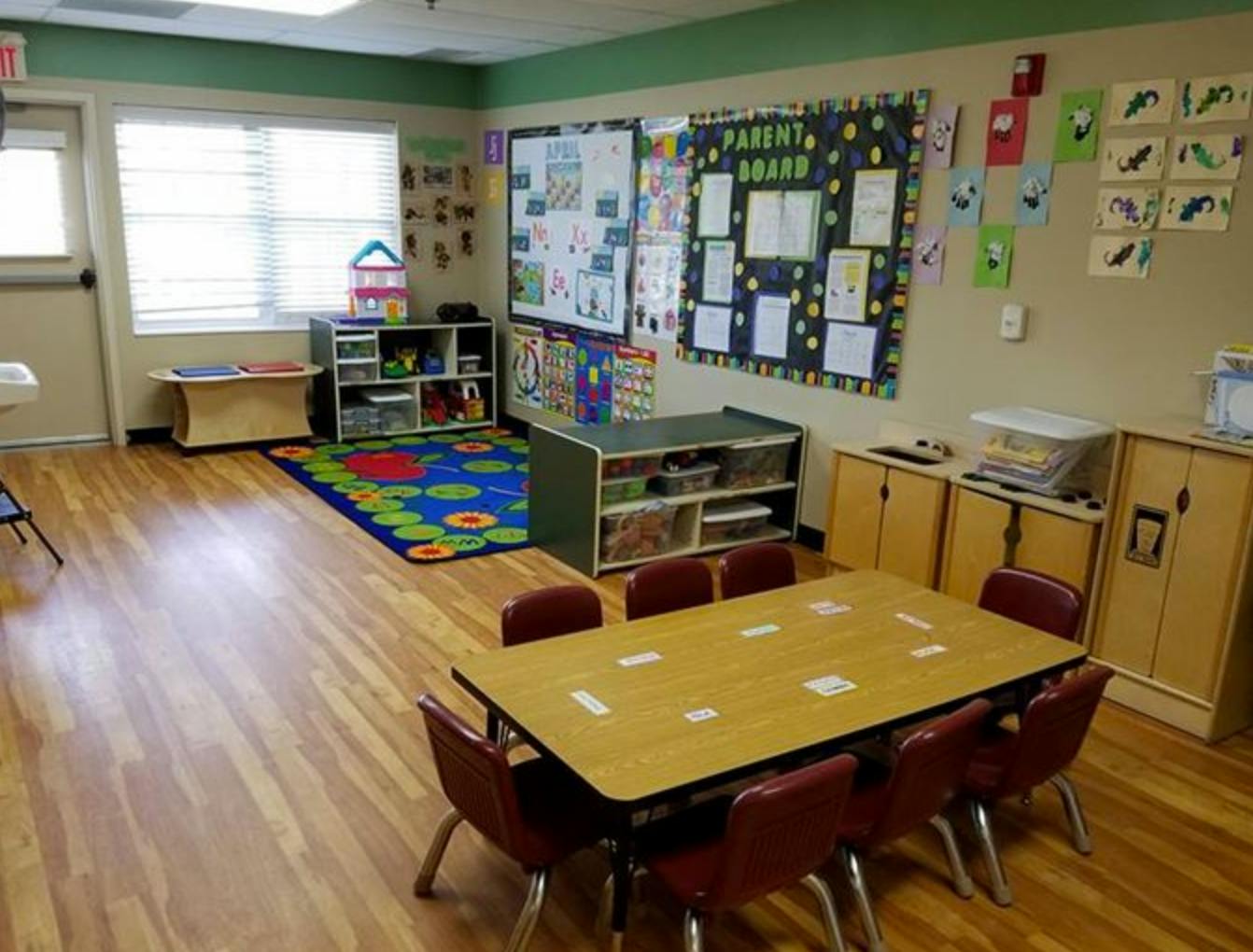 Classroom with small tables and chairs, colorful rug, and bulletin boards