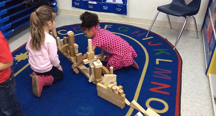Two children playing with wooden blocks on an alphabet rug
