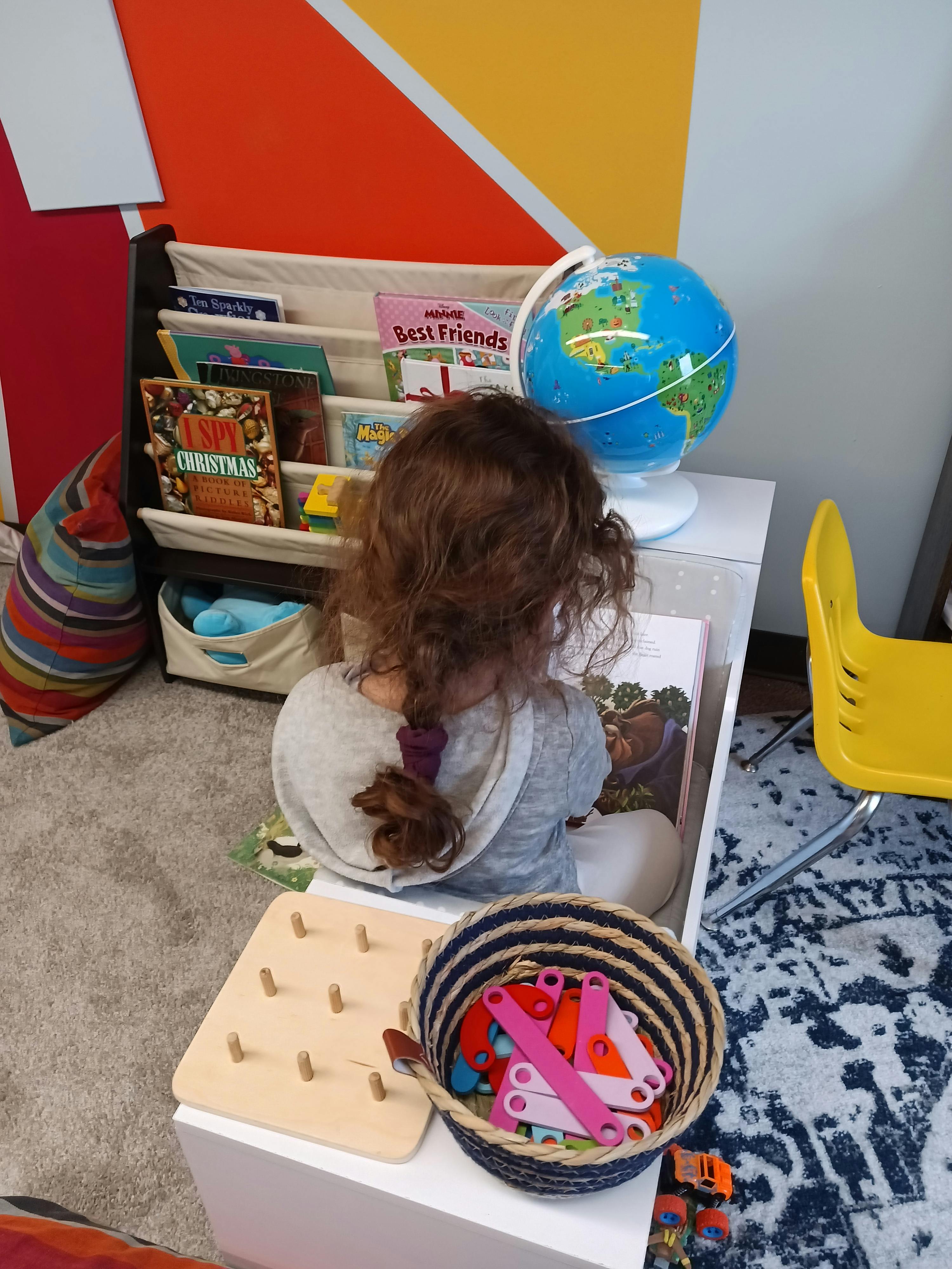 Child looking at a book next to a globe and book shelf