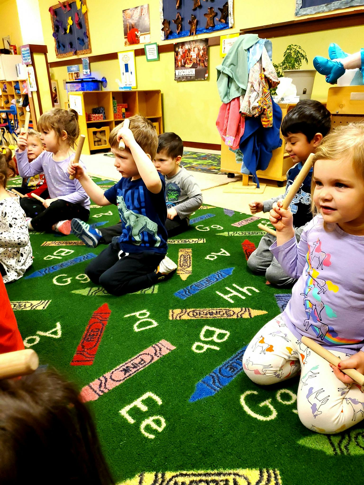 Children sitting on a green rug with crayon and letter patterns