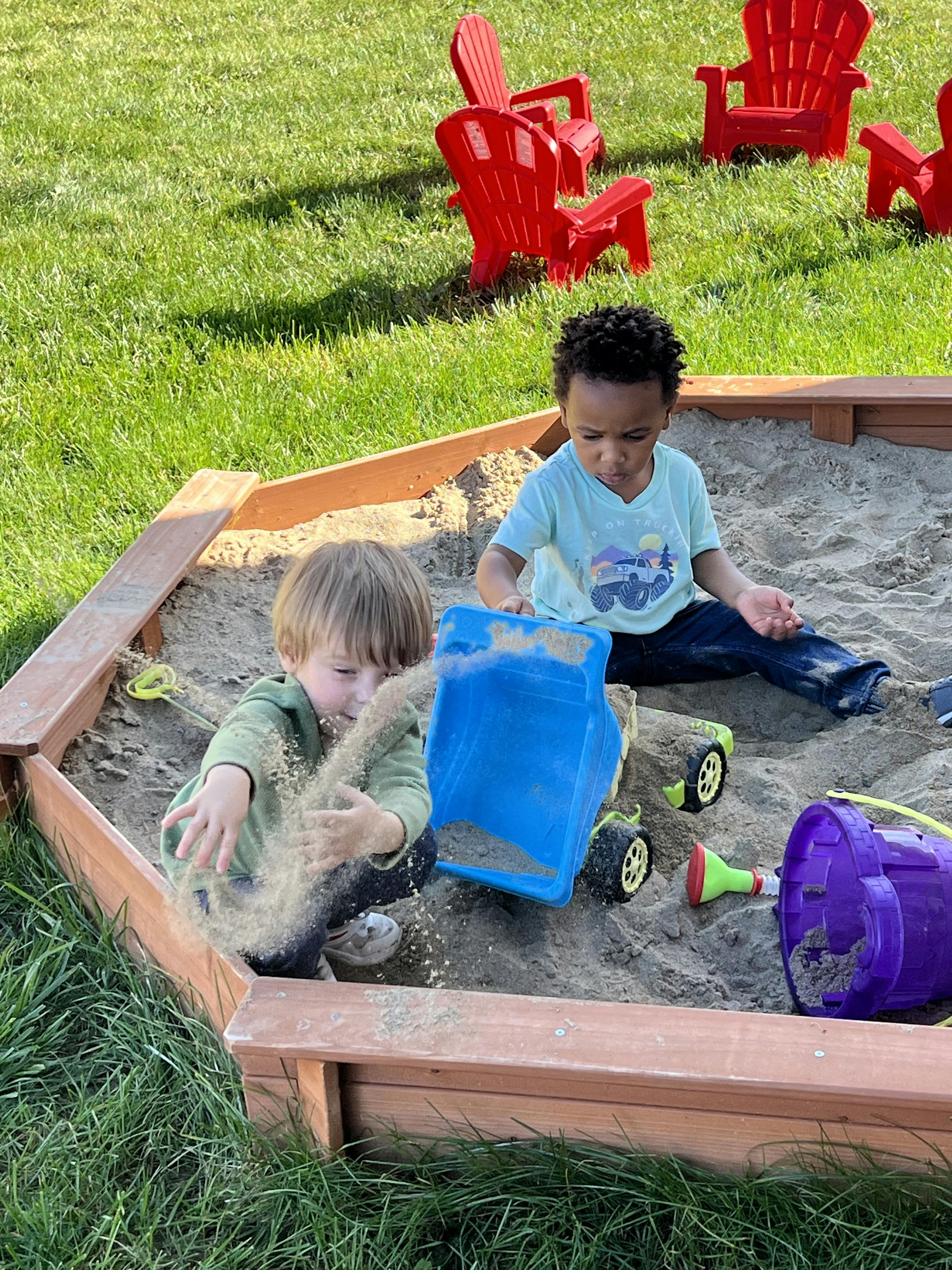 Two children playing with toys in a wooden sandbox