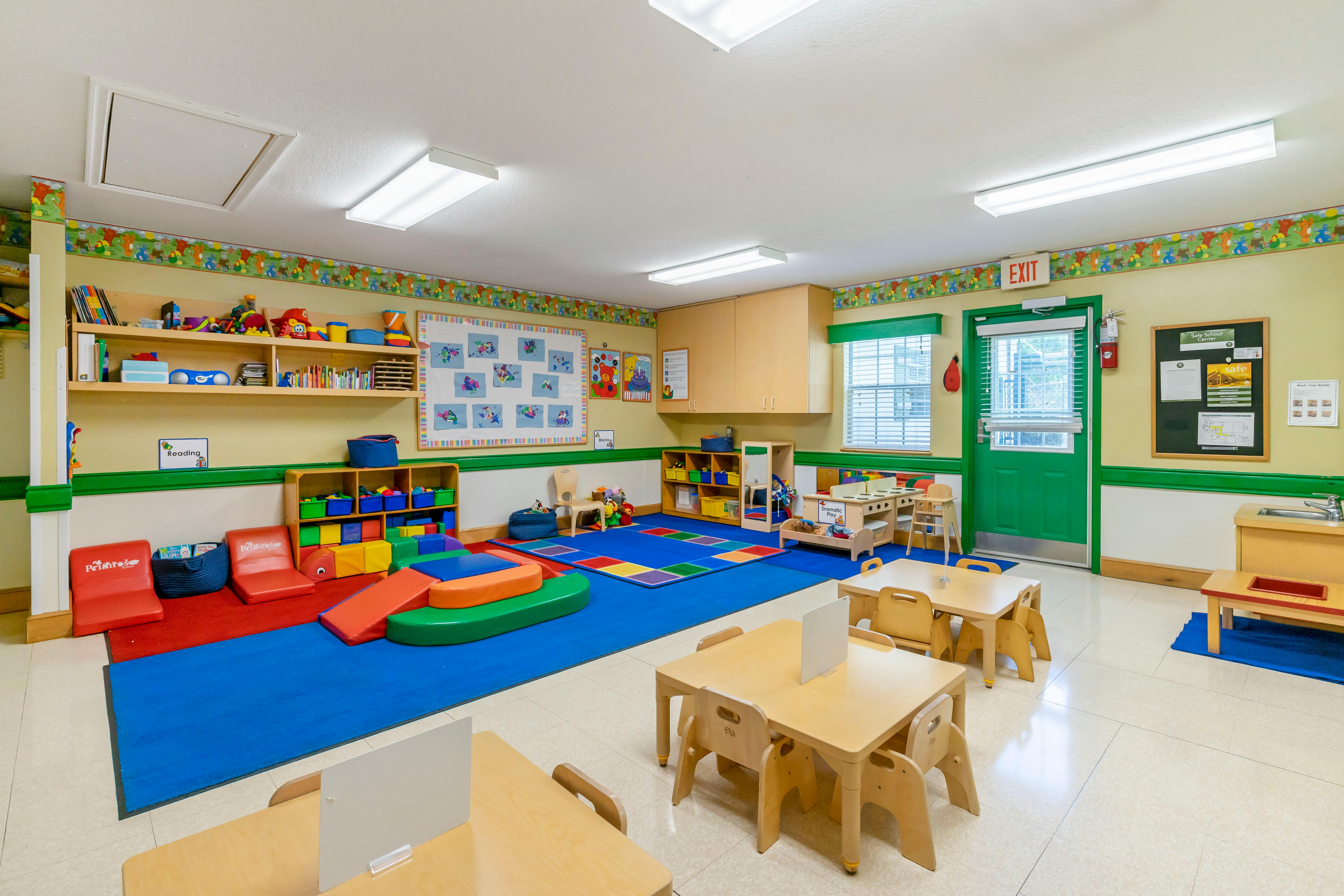 A colorful empty classroom with small tables, chairs, shelving units, and play areas