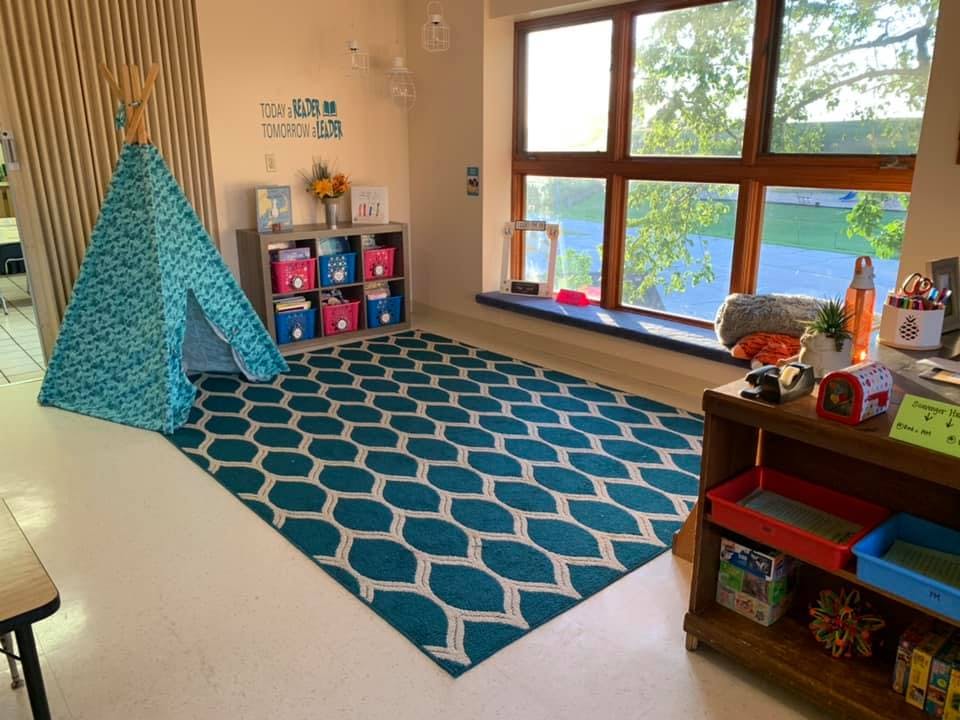 Classroom corner with a blue teepee, patterned rug, and large window