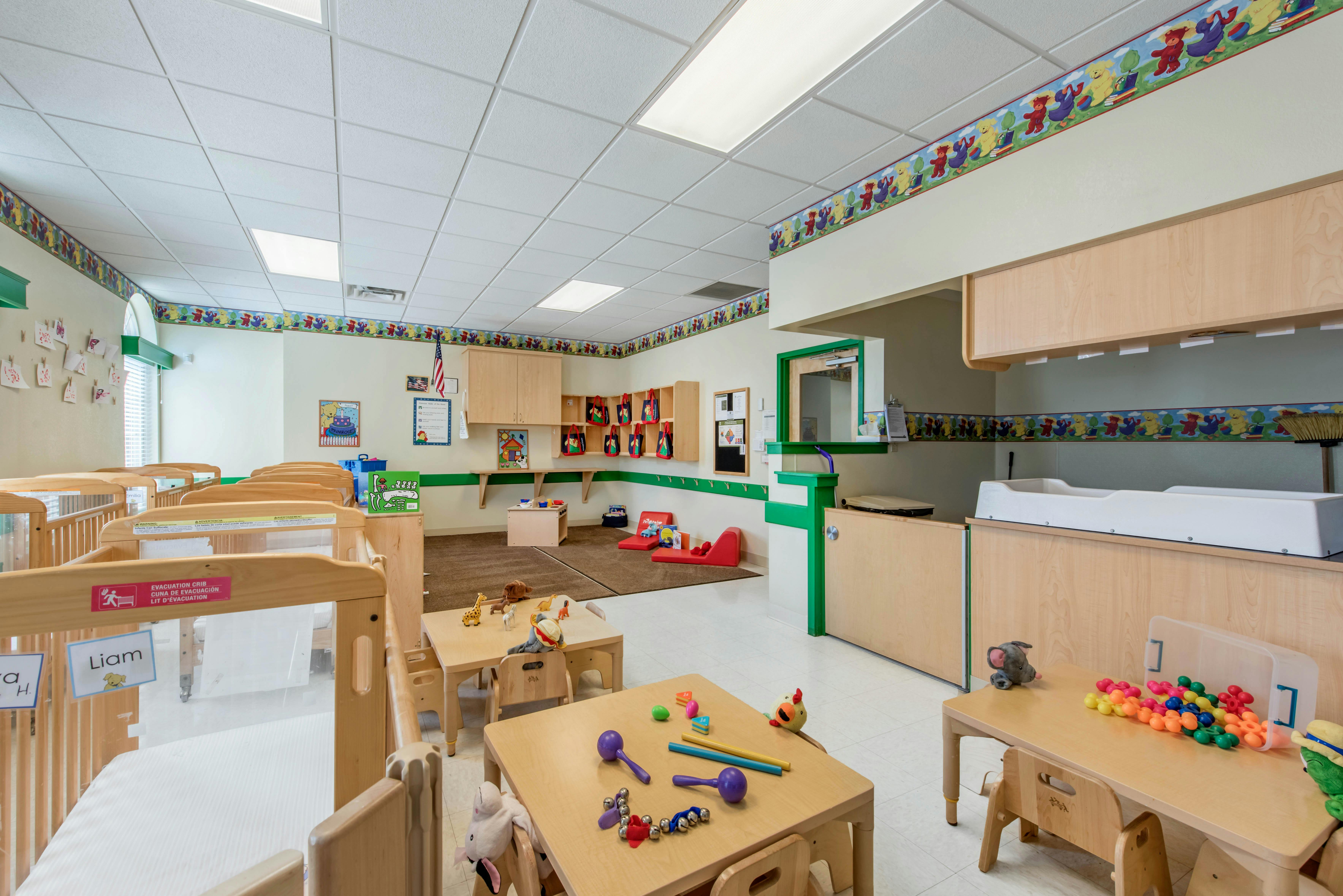 Classroom with multiple cribs, small tables with toys, and a changing station
