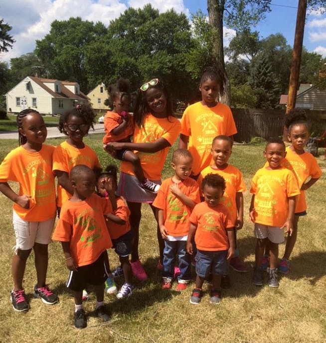 Group of children and adults in orange shirts standing on grass