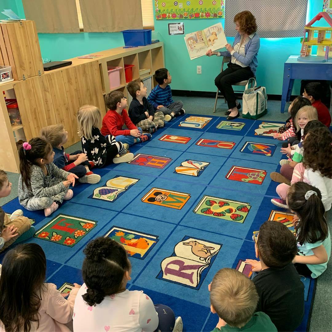 Adult reading a book to a group of children sitting on a rug