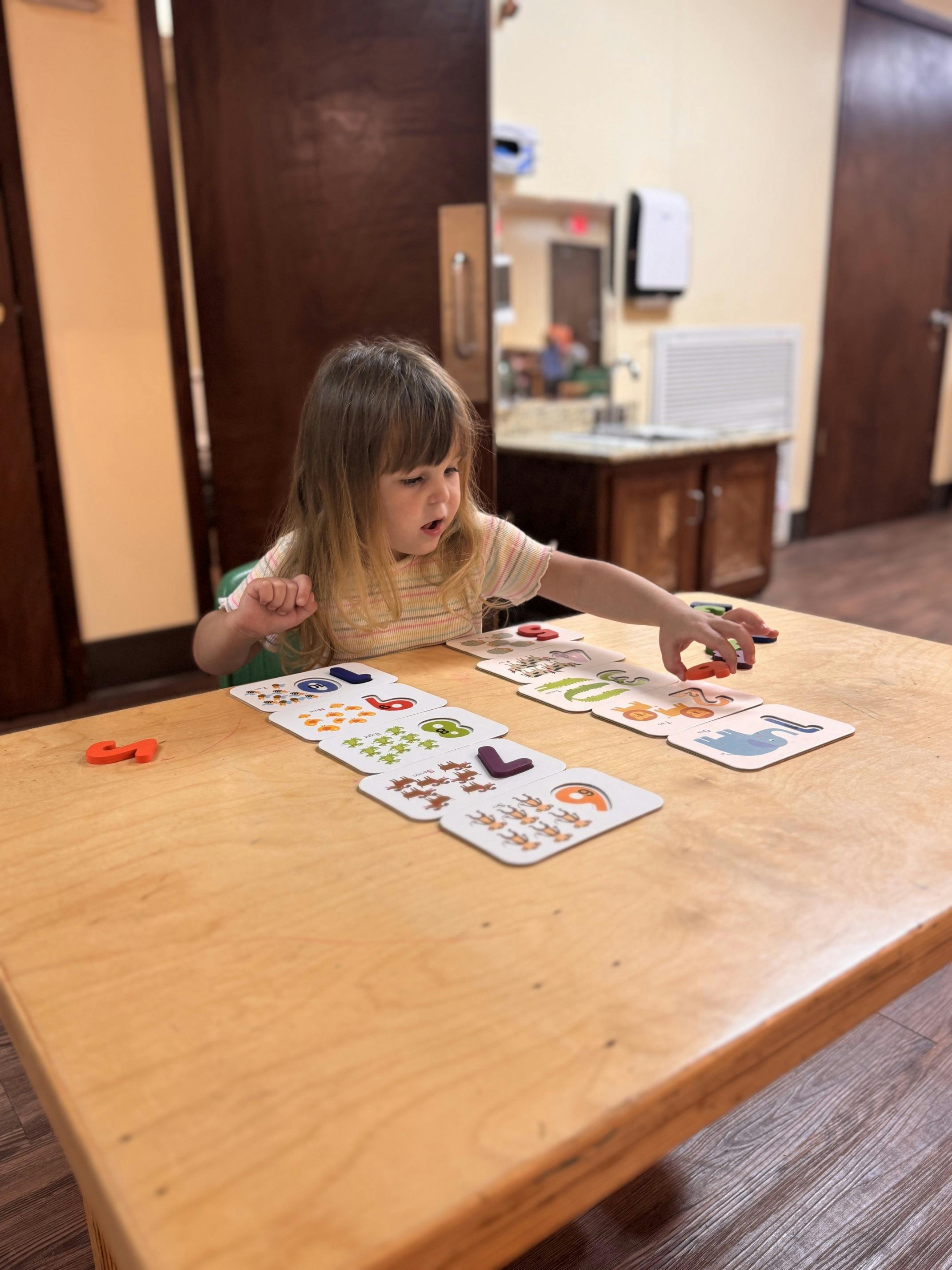 Child playing with number and animal learning cards at a wooden table