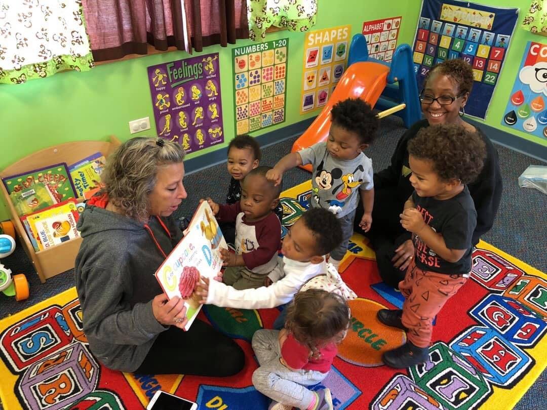 Two adults reading to a group of young children in a classroom