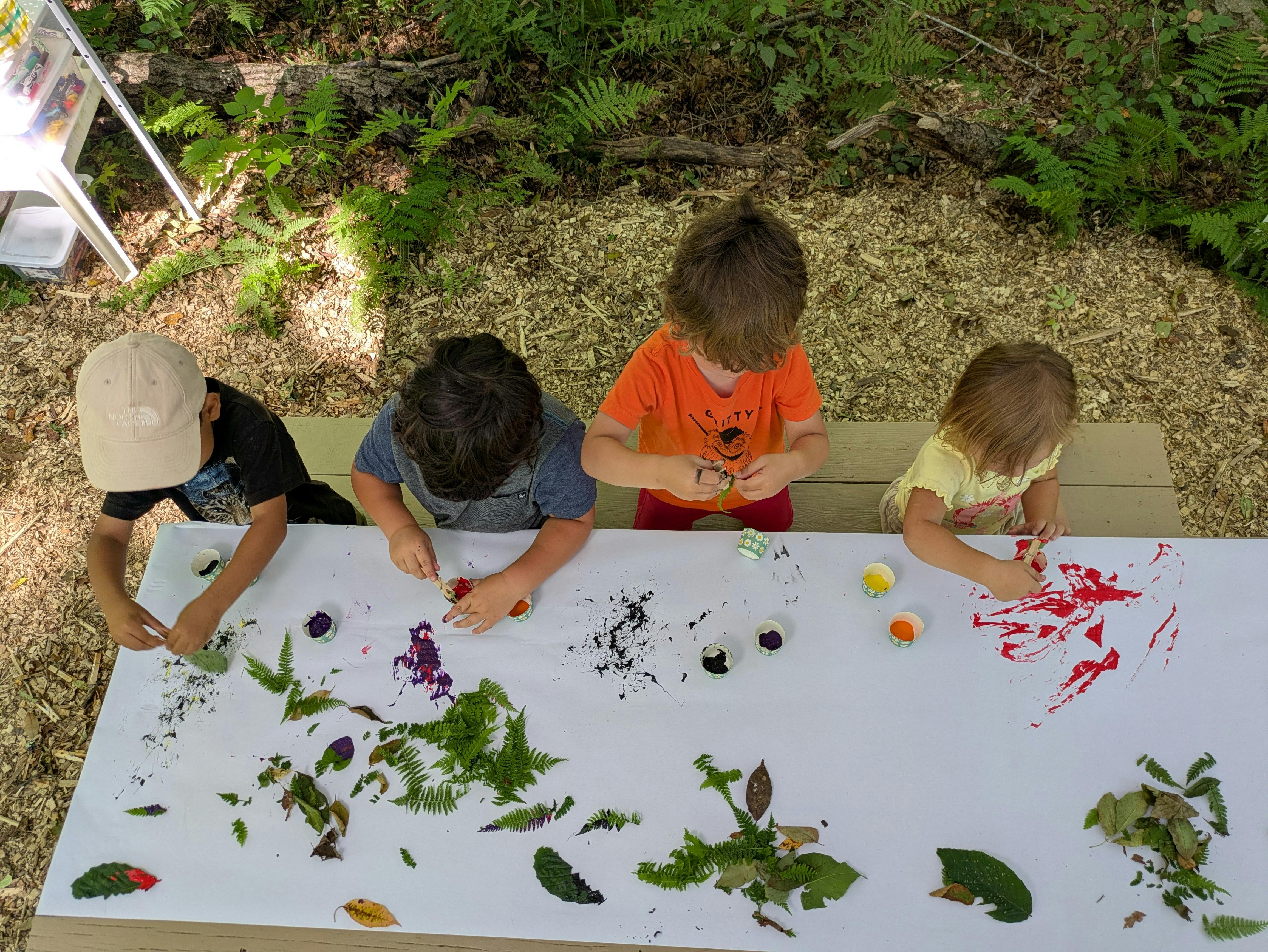 Four children doing nature-based art at a table outdoors
