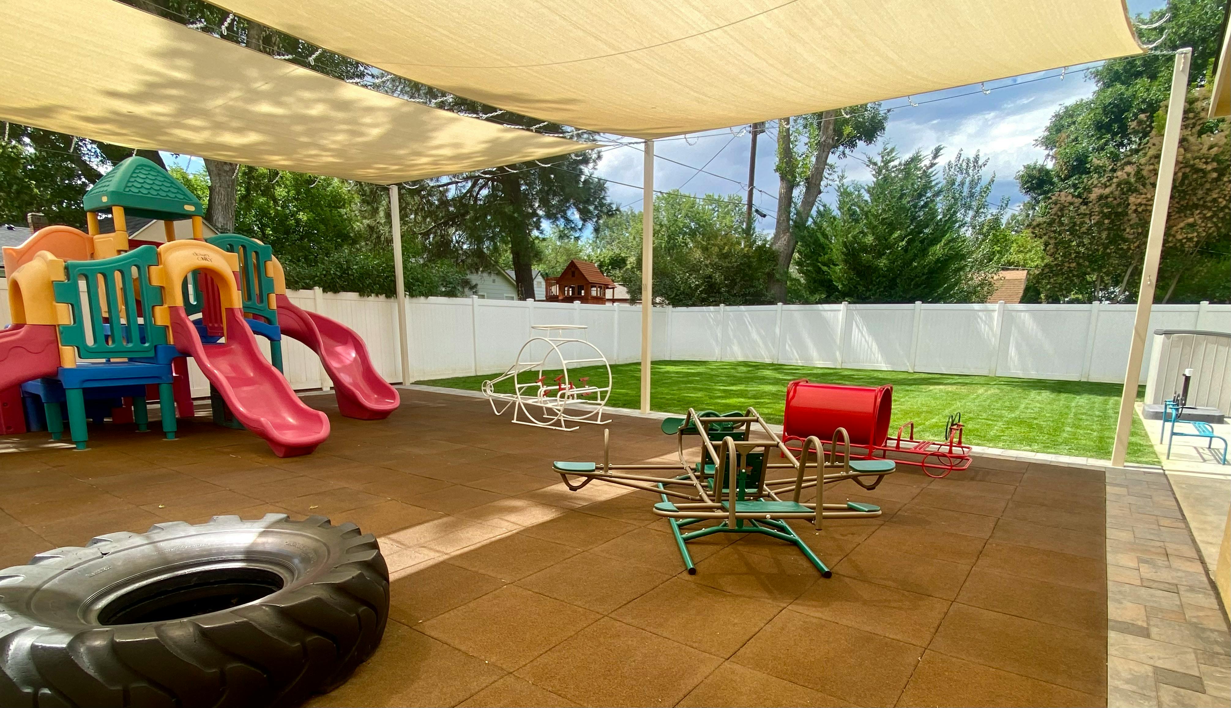 Outdoor playground with slides, swings, and a tire under a shade canopy