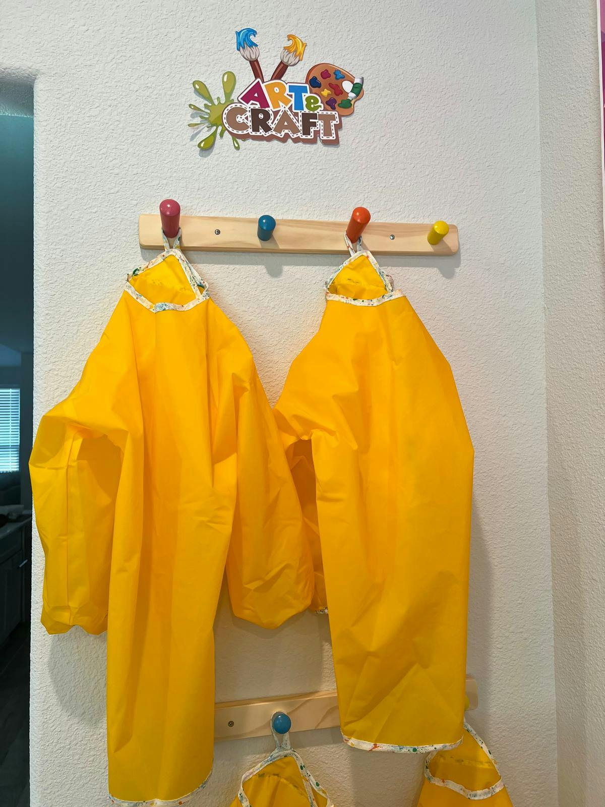 Yellow smocks hanging on a wall rack below an "Art & Craft" sign