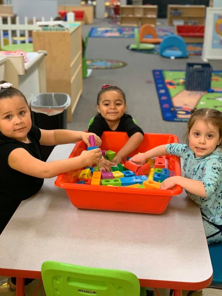Three children playing with colorful building blocks in a classroom
