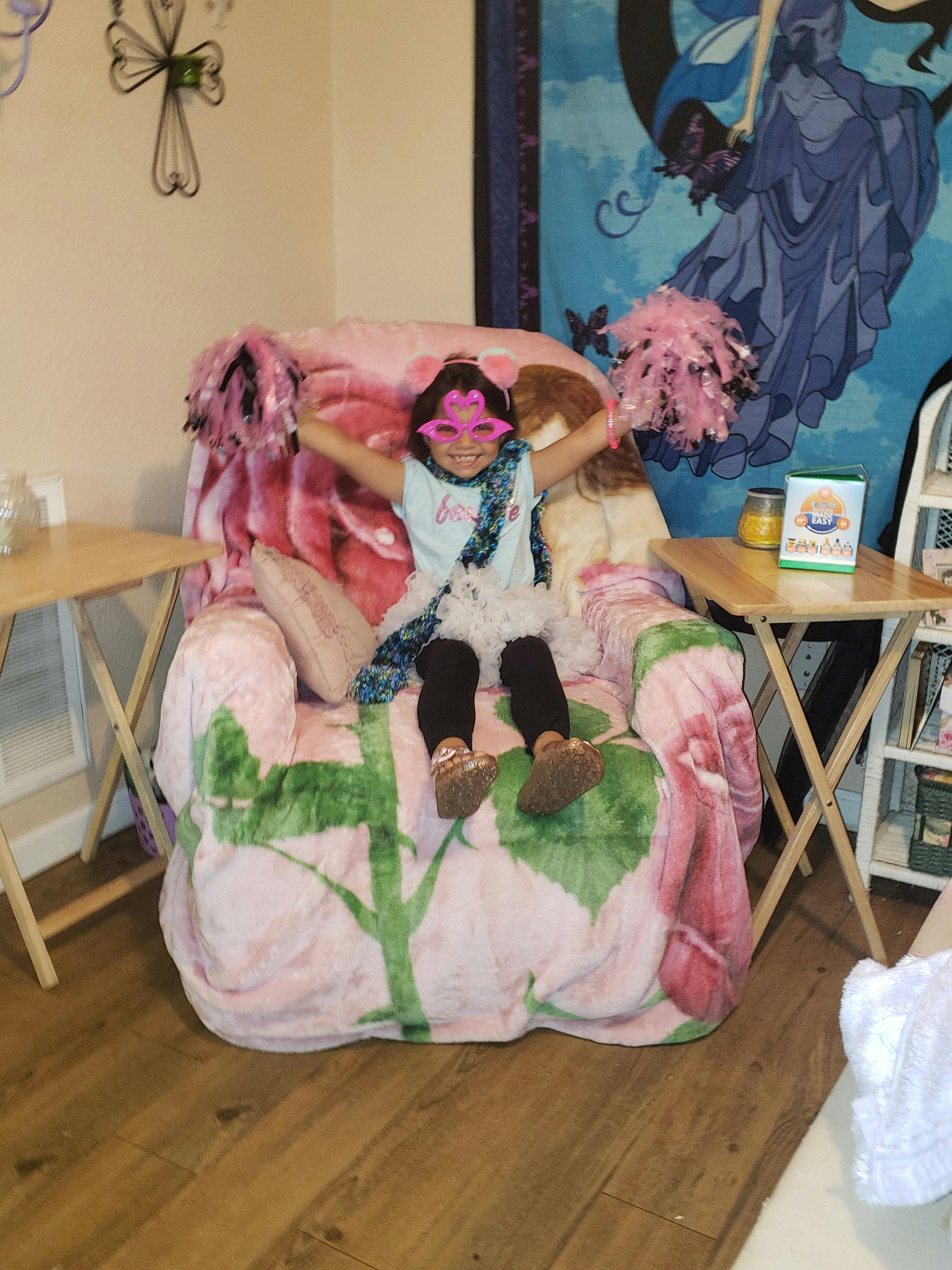 Child wearing star-shaped glasses sitting in a large armchair with arms raised