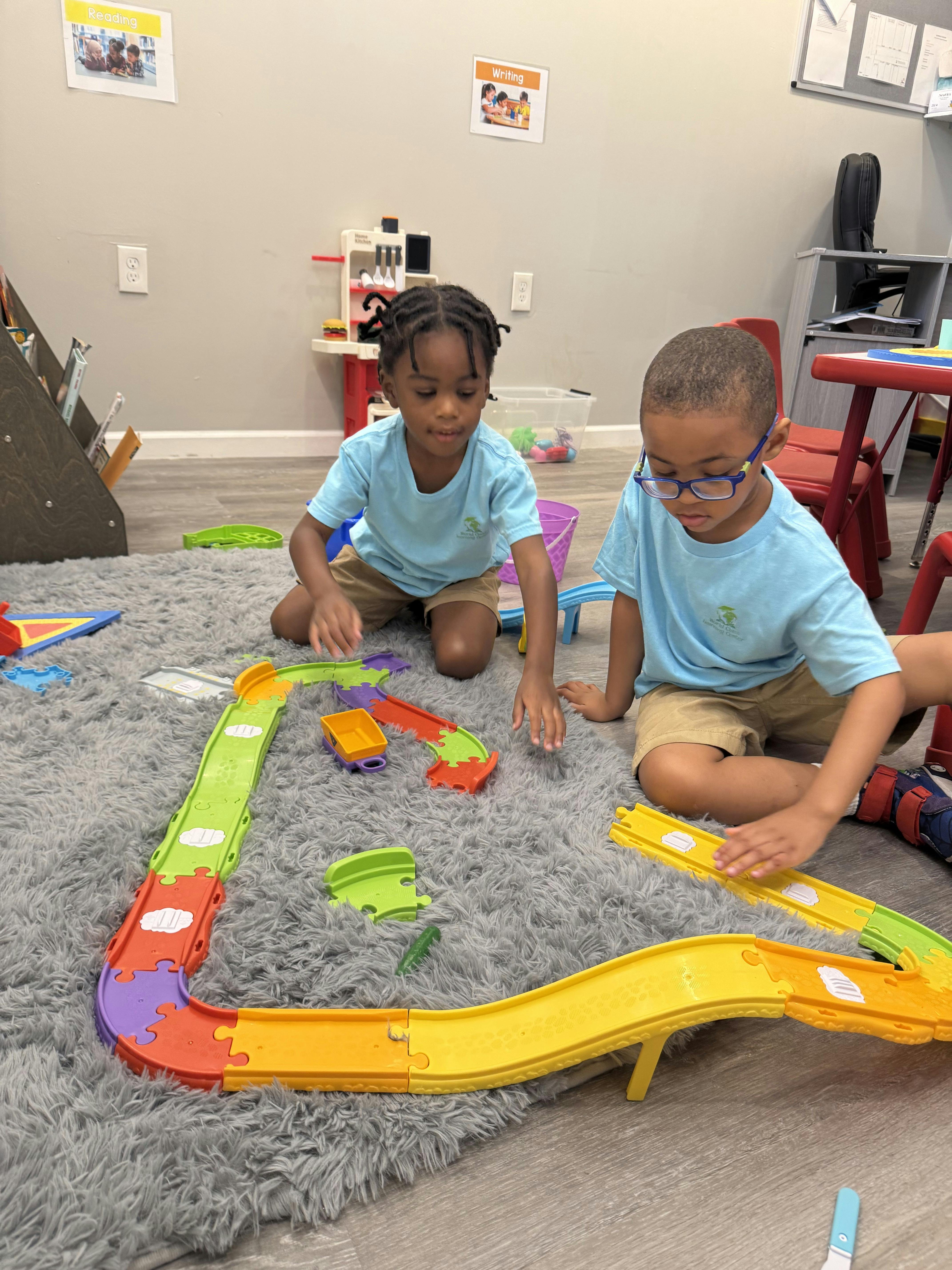 Two children playing with a toy car track on a rug