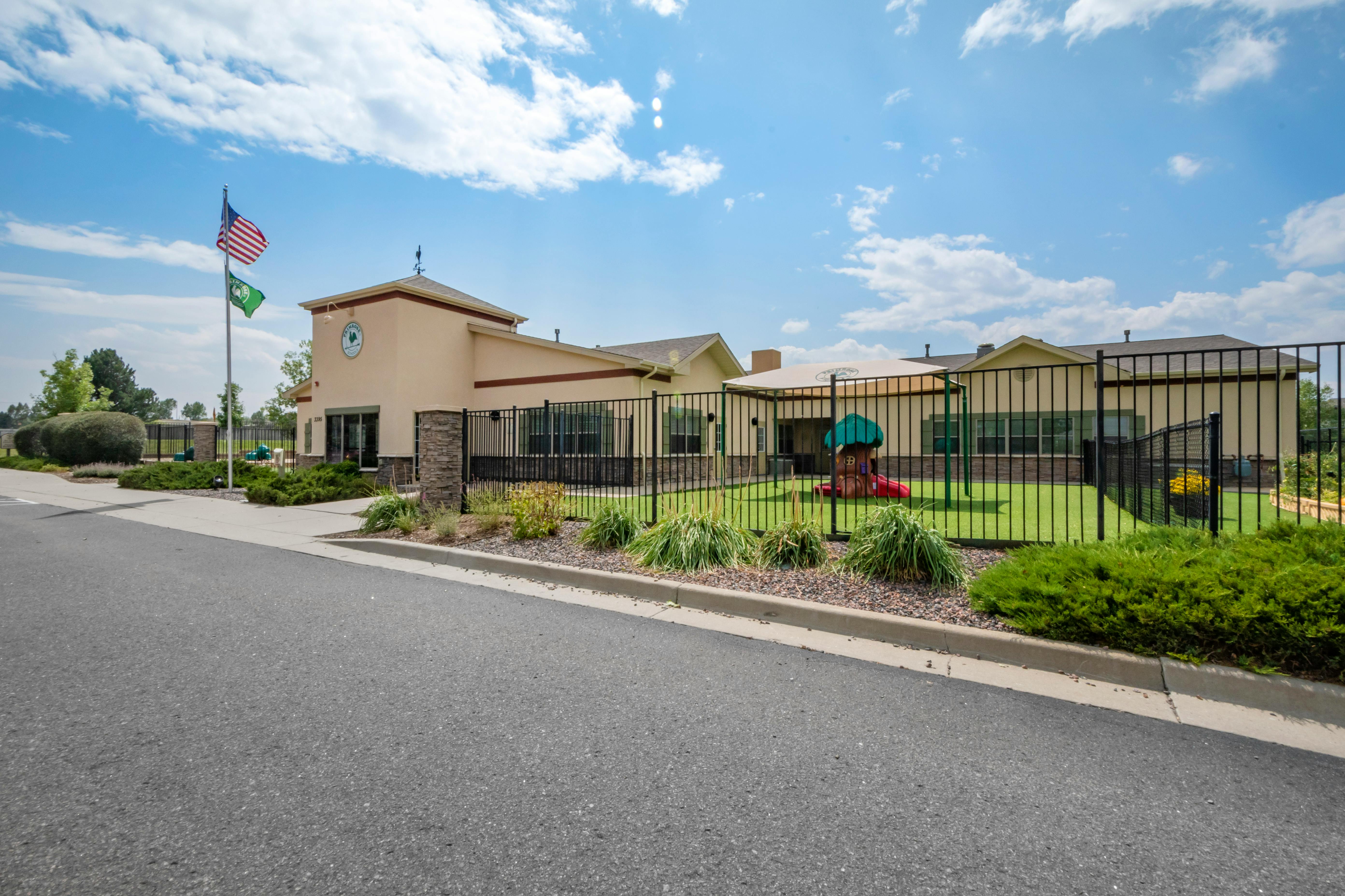 Exterior view of a school building with a fenced playground and flags