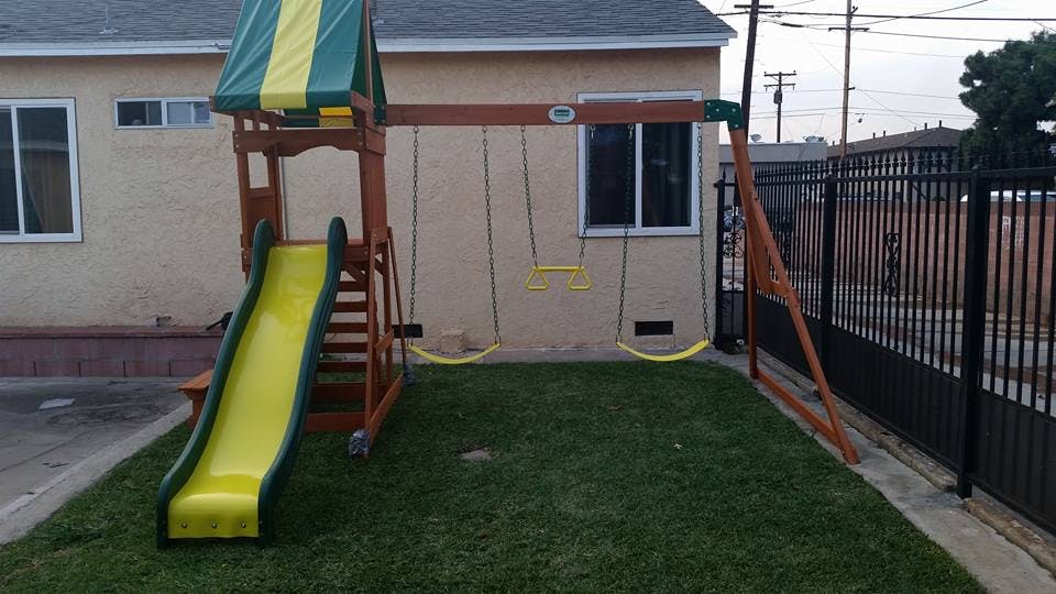 Playset with a yellow slide and swings in a grassy yard