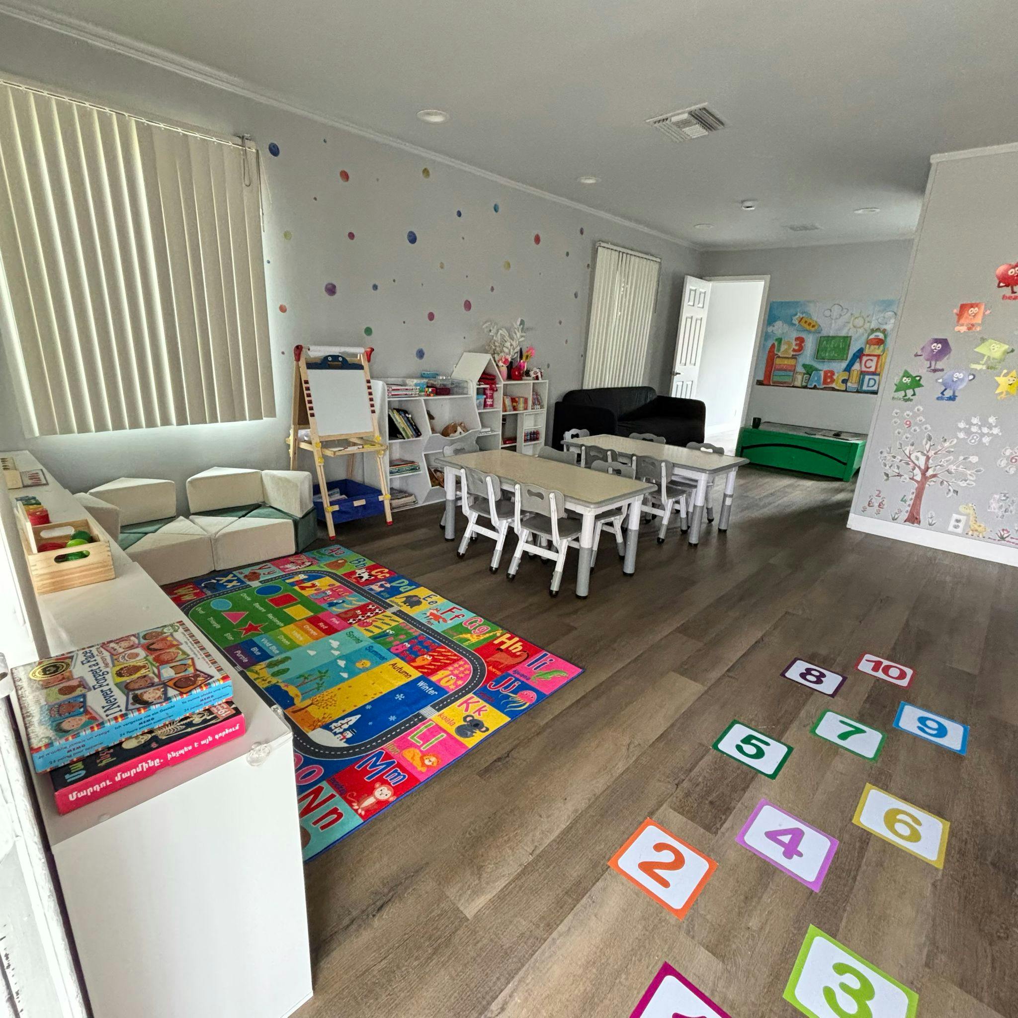 A classroom with small tables and chairs, a colorful alphabet rug, and number cards on the floor
