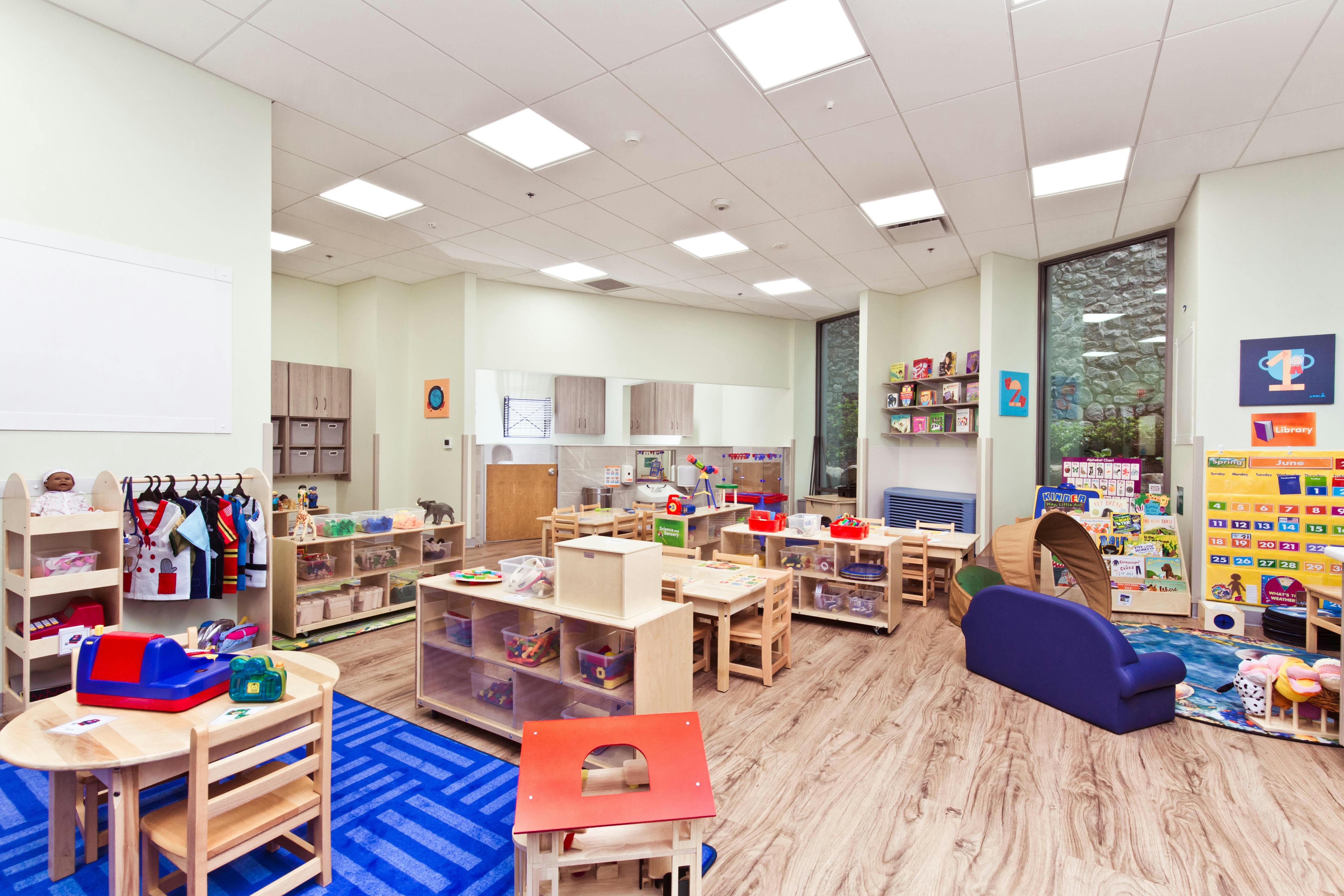 Classroom with child-sized tables and chairs, shelves with toys, and a dress-up rack
