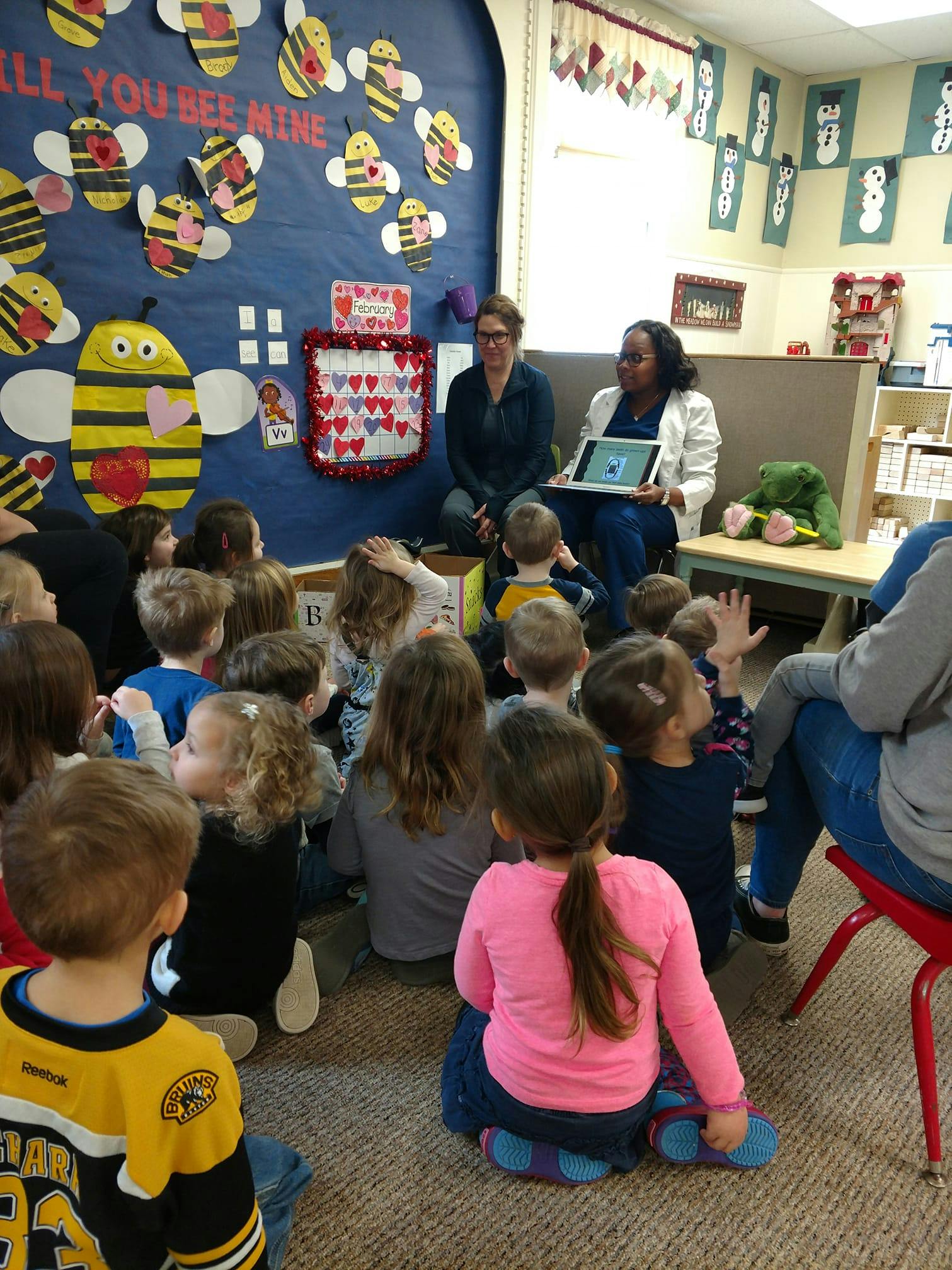 Two people presenting to a group of children sitting on the floor in a classroom