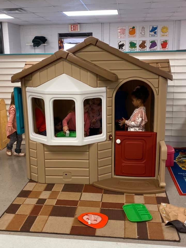 Children playing in and around a toy playhouse in a classroom